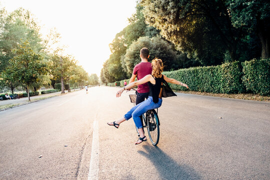 Young woman with arms outstretched sitting with boyfriend on bicycle in park