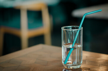 A glass of water with Green drinking straw on wood table background in restaurant.