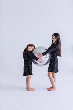 Sibling holding disco ball together while standing against white background in studio