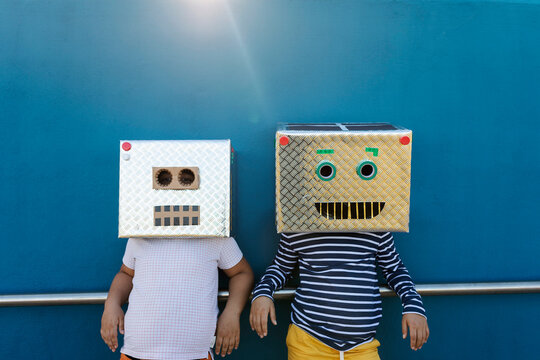 Friends wearing robot costumes made of boxes while standing against blue wall