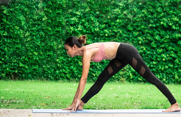 Fototapeta premium Morning outdoor garden grass green park natural holiday female model trainer slim fit sixpack body wear sport bra is playing yoga balance workout fitness class excercise for health care insurance 