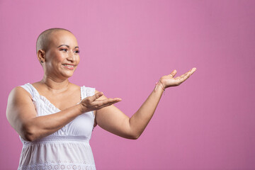 Mujer con cáncer de mama en fondo rosado señalando a un lado - obrazy, fototapety, plakaty