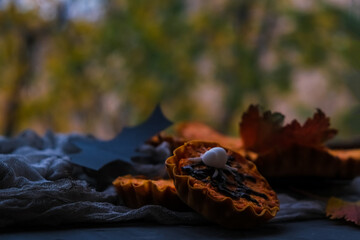 bright orange cupcakes in tartlets with a spider on background of gray web. next to autumn leaves. concept of Halloween