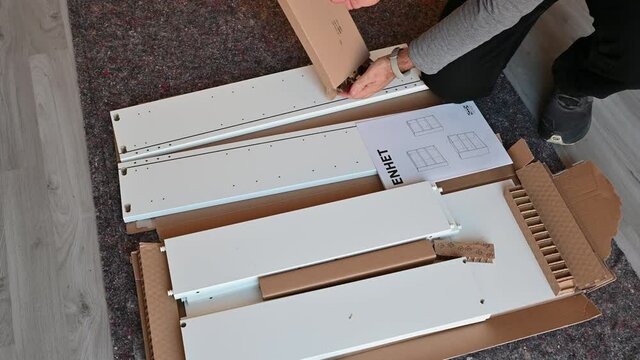 Turin, Italy. October 2020. Scenes at home: assembly of a piece of furniture, the Caucasian man takes the small parts out of the box and checks the quantity. Next to the assembly manual.