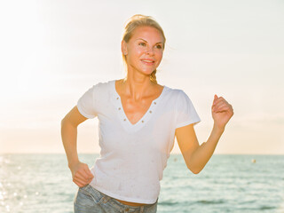 Female in white T-shirt is jogging on the beach.