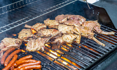 Tomahawk rib beef steak ans sausages on hot black grill with flames bbq