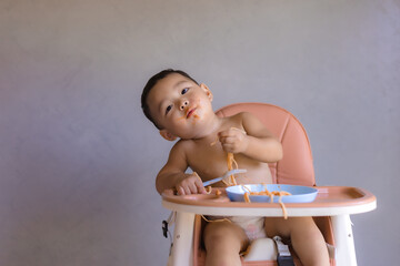 Asian boy eatting on high baby chair.