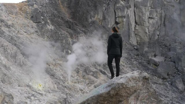 Woman standing on rock looking at sulfur smoke from volcano in North Sumatra, Indonesia