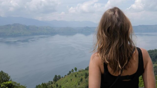 Ultra slow motion shot of young caucasian woman looking at Lake Toba from Samosir Island in North Sumatra, Indonesia