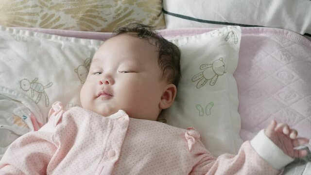 2 month old mixed asian baby lying in bed happily watching an electronic mobile rotate.