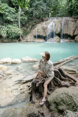 Woman sitting on the stone at Erawan waterfall at National Park, Kanchanaburi, Thailand.