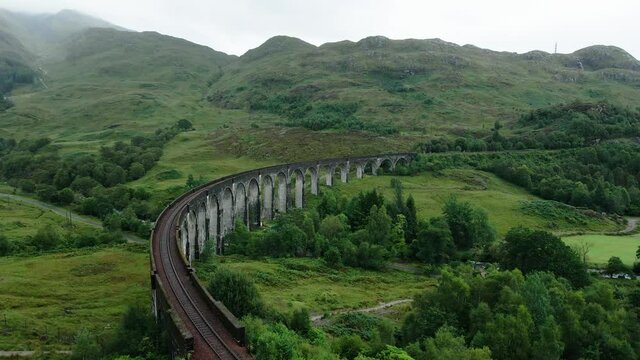 Glenfinnan Viaduct Surrounded By The Lush Green Mountains At Early Morning In The Highlands Of Glenfinnan, Scotland, UK. Railway On The West Highland Line - aerial drone, Mavic Air 2