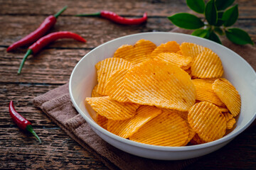 Spicy potato chips in white bowl and chili on wooden table