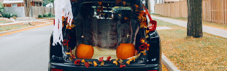 Trick or trunk. Black car trunk decorated for Halloween. Autumn fall decor with red pumpkins and yellow leaves for traditional October holiday outdoors. Web banner header.