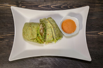 A spinach wrap with chicken and dipping sauce on the side.