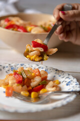 Close up of a hand holding a spoon full of macaroni cheese pasta onto a plate