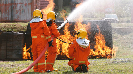 Naklejka premium Firefighter fighting with flame using fire hose chemical water foam spray engine. Fireman wear hard hat, body safe suit uniform for protection. Rescue training in fire fighting extinguisher