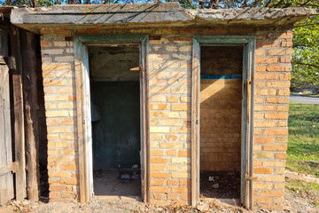 abandoned old brick toilet with two doors at sunny day.