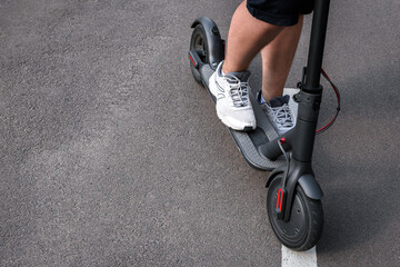Close-up of a man standing on an electric scooter on the background of an asphalt road © thomsond