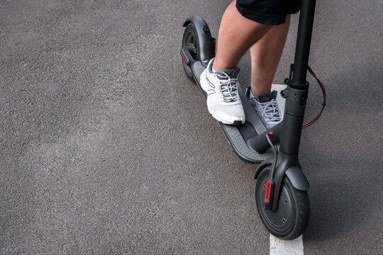 Close-up of a man standing on an electric scooter on the background of an asphalt road