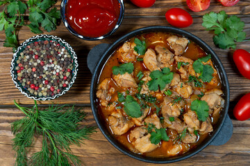 Meat stewed with herbs and spices, condiments, cherry tomatoes, dill and parsley, top view on a wooden table. Homemade food.