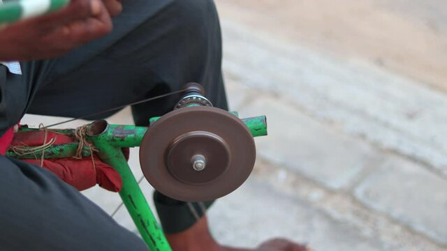 Closeup man sharpening gardening scissors on a makeshift mobile sharpening machine on a manual bicycle frame.