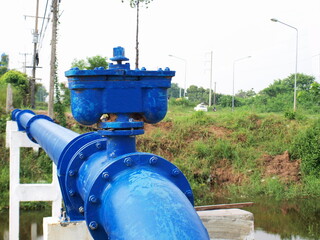 Fototapeta na wymiar Dual air valve on blue plumbing. Serves to ventilate and prevent water pipes from being damaged by vacuum. On the background of the water canal, green trees and white sky. Selective focus