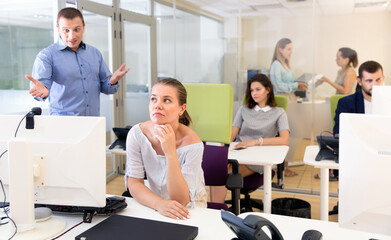 Upset unhappy girl sitting at laptop in coworking space while angry businessman pointing out mistakes in her work