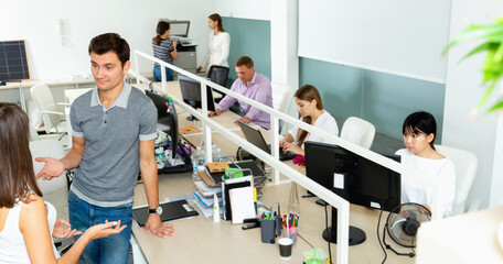 Glad positive smiling male and female office co-workers having conversation at desk in office