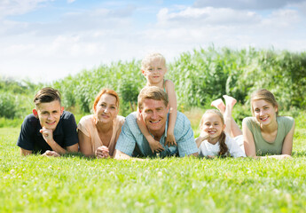 Fototapeta premium happy smiling mature man and woman with four children lying on the grass in park on summer day.