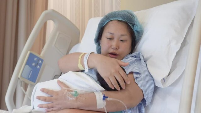 An Asian women holds her baby in the recover suite for the first time after giving birth gazing at her. 