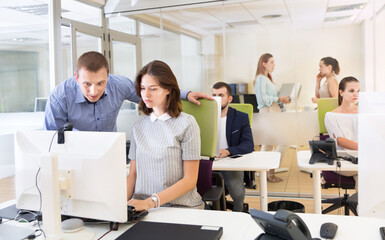 Experienced businessman helping female colleague in work with computer in the modern coworking space