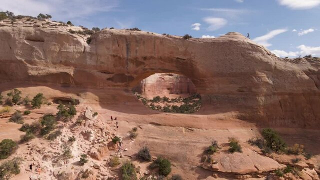 Group Of Travelers Climbing The Amazing Red Rock Formation Known As Wilson Arch, A Roadside Attraction In Moab, Utah, United States - Wide Shot Pan Left