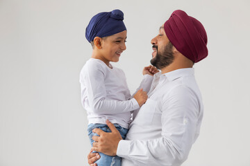 A LITTLE SIKH BOY LOOKING AT HIS FATHER AND SMILING	