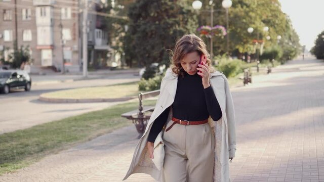 Young stylish woman walks confidently down the street and speaks on the phone. Business style of a modern woman.