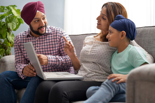 A SIKH PARENTS LOOKING AT EACH OTHER WHILE TEACHING SON WITH LAPTOP	