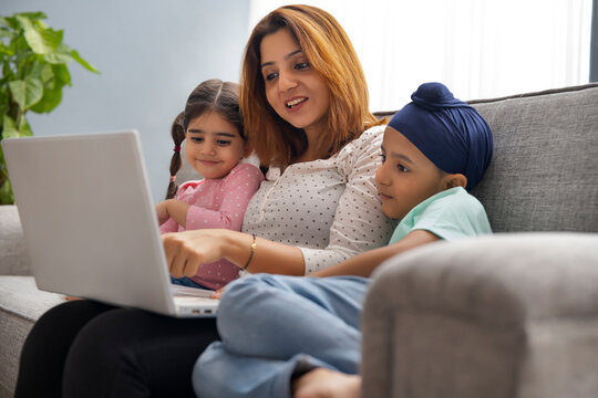 A SIKH MOTHER CHEERFULLY TEACHING HER SON AND DAUGHTER ON A LAPTOP AND KIDS LARNING CAREFULLY
