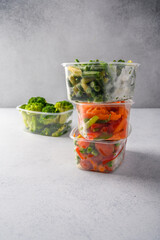 Frozen vegetables carrot, broccoli, spinach, green pods beans in plastic trays on light background, selective focus concept diets and healthy eating with copy space