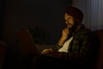 A SIKH MAN THINKING WHILE WORKING ON LAPTOP AT NIGHT	
