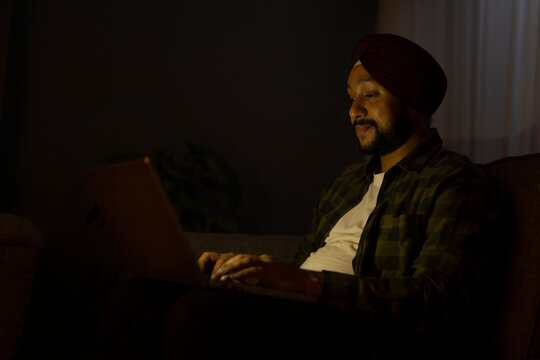 A SIKH MAN SITTING AND WORKING ON LAPTOP DURING NIGHT	
