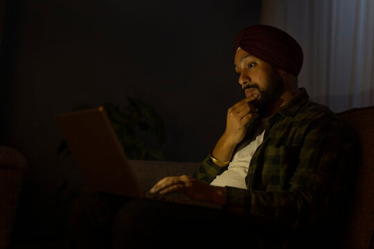 A SIKH MAN THINKING WHILE WORKING ON LAPTOP AT NIGHT	 - Powered by Adobe