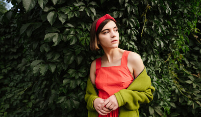 Portrait of beautiful young woman staying in green park garden trees  natural background. Red dress...