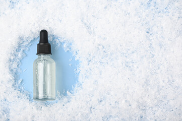 Glass bottle with serum, essential oil on blue background on the snow. Gentle moisturizing skincare...