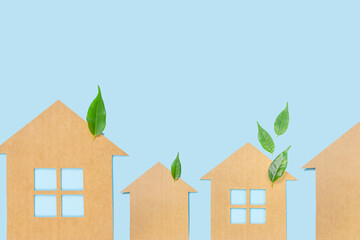 Houses made of craft paper and green leaves of a plant on a light blue background. Eco-friendly home concept, healthy lifestyle, zero waste...