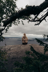 Women girl sitting on the rock cliff and watching clouds above the lake and tree branch in Finland