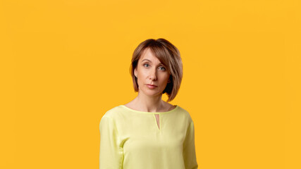 Obraz premium Confident mature woman. Female lifestyle. Success independence. Portrait of elegant lady in yellow blouse with short hair looking at camera isolated on orange copy space commercial background.