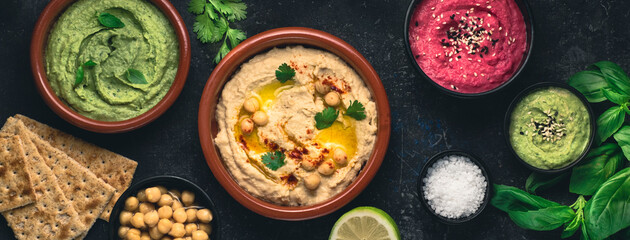 Flat lay of the various types of vegetarian hummus based on herbs, basil and coriander on a dark rustic background, moke up. Healthy vegetarian food concept, vegetable proteins