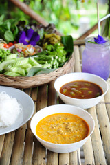Thai Food Rice Noodles in Fish Curry With fish balls, pork snack, basil, bean sprouts on top, placed on a wooden table.