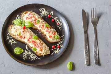 Fried eggplant stuffed with tomatoes, grated cheese, yogurt dressing and cranberries, garnished with Basil leaves on a dark plate over gray slate, stone or concrete.Top view.