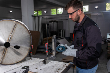 Industrial worker with angle grinder working on metal structure at workshop.	